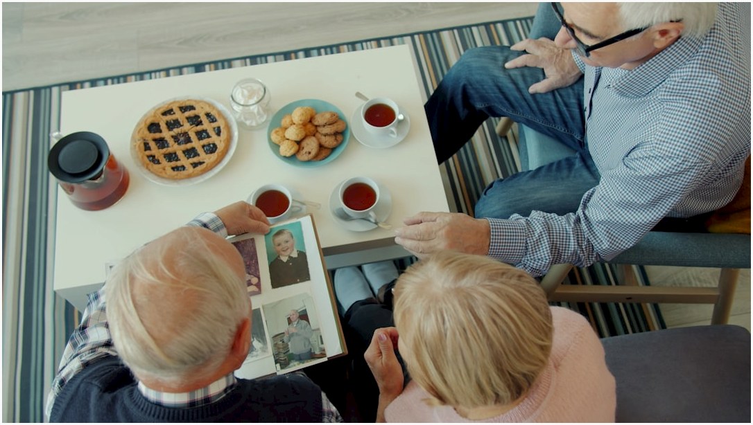 Seniors looking at a photo album with tea and snacks.
