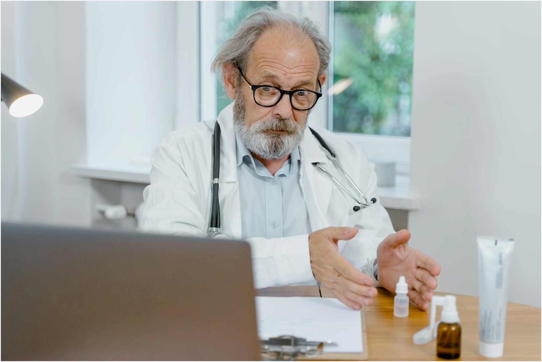 An elderly doctor in a white coat conducting an online medical consultation, focusing attentively.