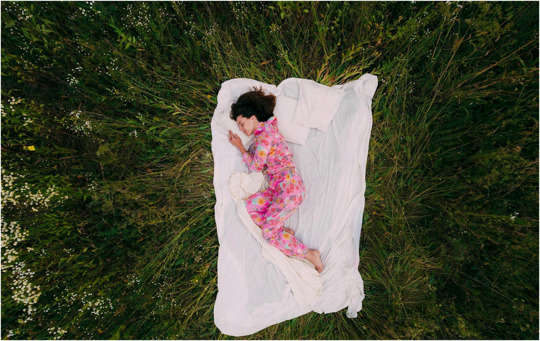 Woman in floral pajamas peacefully napping outdoors on a blanket in a grass field.