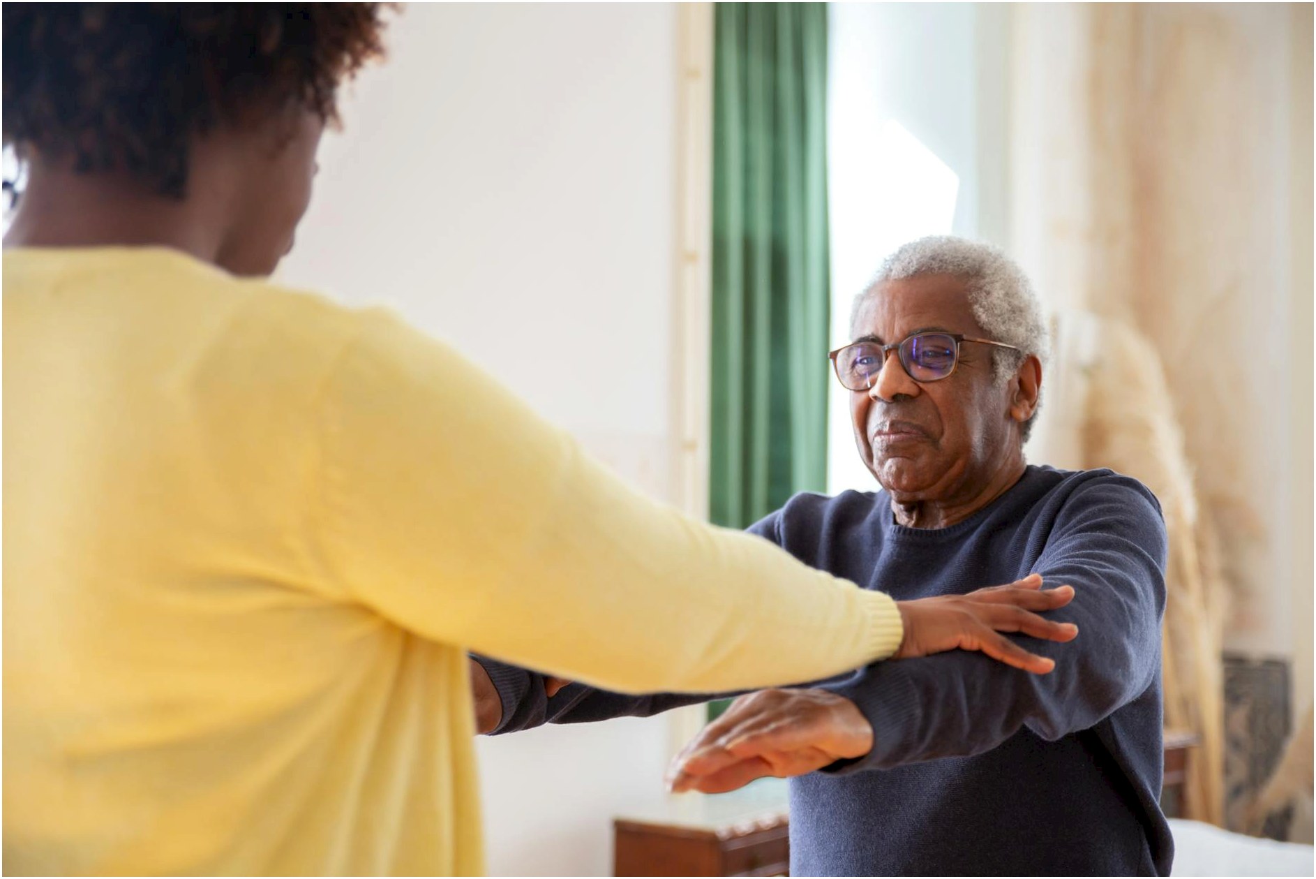 An elderly man with a caregiver assisting him in exercise at home.