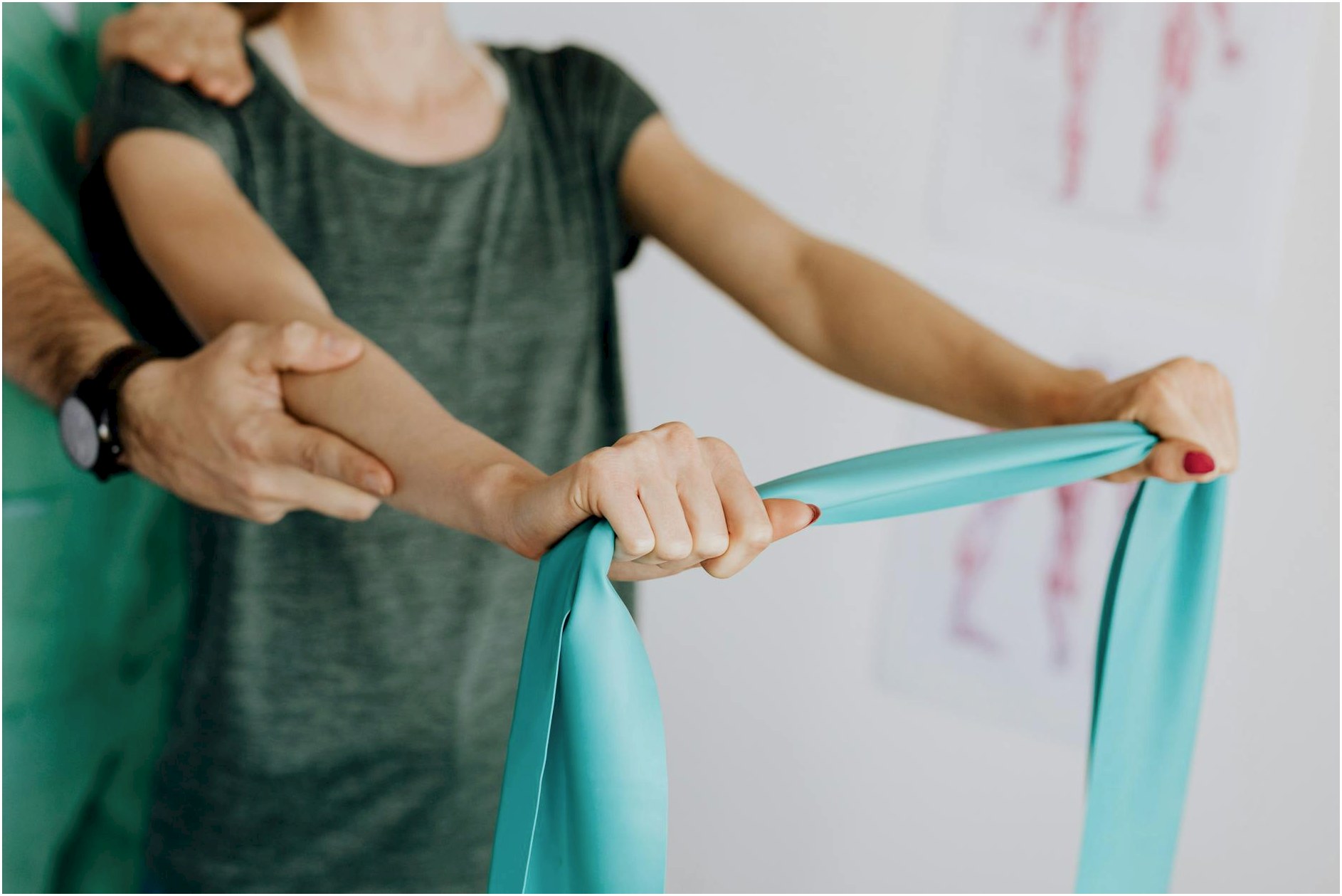 Crop unrecognizable orthopedist in uniform and wristwatch supporting shoulder and reached arm of faceless female patient with resistance band in doctor office