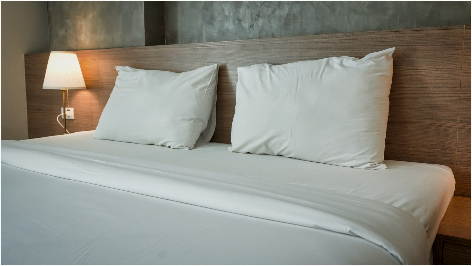 A clean and contemporary hotel room featuring minimalist bedding and a warm bedside lamp.