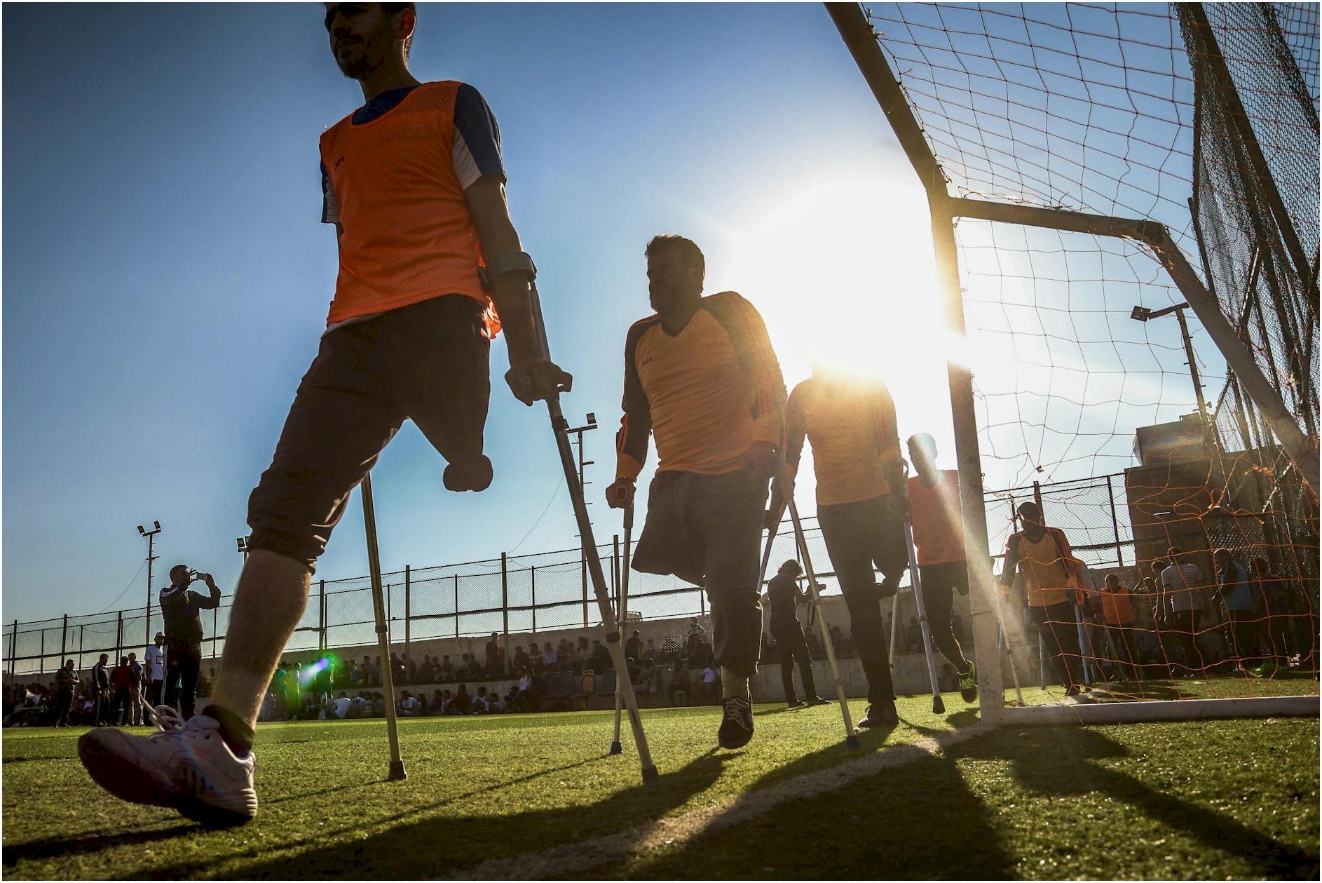 Amputee soccer players in orange jerseys competing on a sunny field.