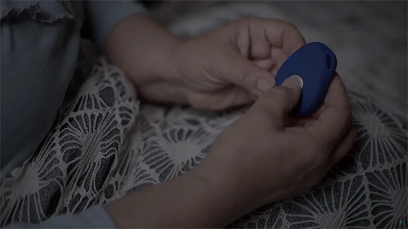 Mãos de uma pessoa idosa acionando um pequeno botão SOS azul