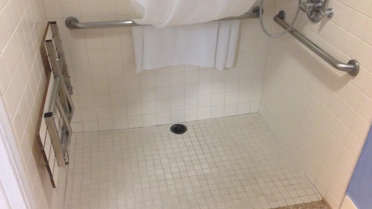 Assento de banho rebatível fixado na parede em banheiro acessível com barras de apoio