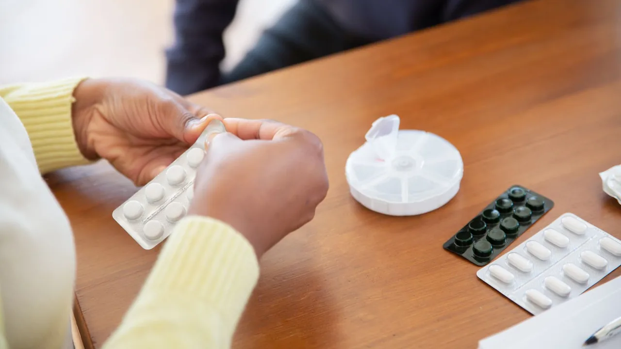 Pessoa idosa organizando medicamentos em casa com apoio de um cuidador