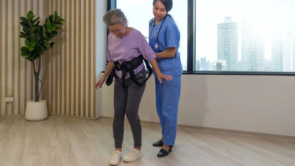 Cuidadora orienta pessoa idosa usando cinto de transferência durante a marcha