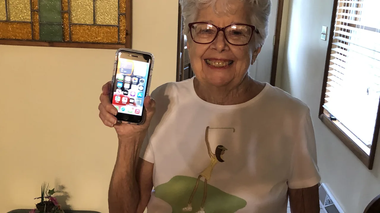 Pessoa idosa mostrando um celular enquanto recebe ajuda para usar o aparelho