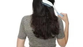 Pessoa usando escova de cabelo com cabo longo para alcançar a parte de trás da cabeça
