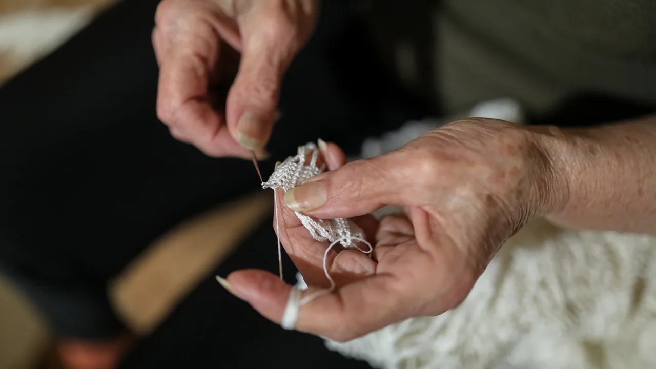 Mãos de uma mulher idosa realizando trabalho manual com linha e agulha