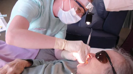 Dentista examina a boca de uma pessoa idosa durante atendimento odontológico
