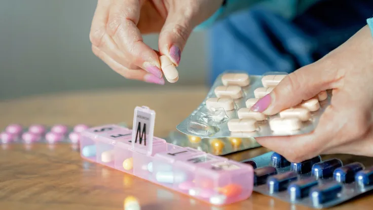 Organizador semanal de medicamentos ao lado de cartelas e comprimidos