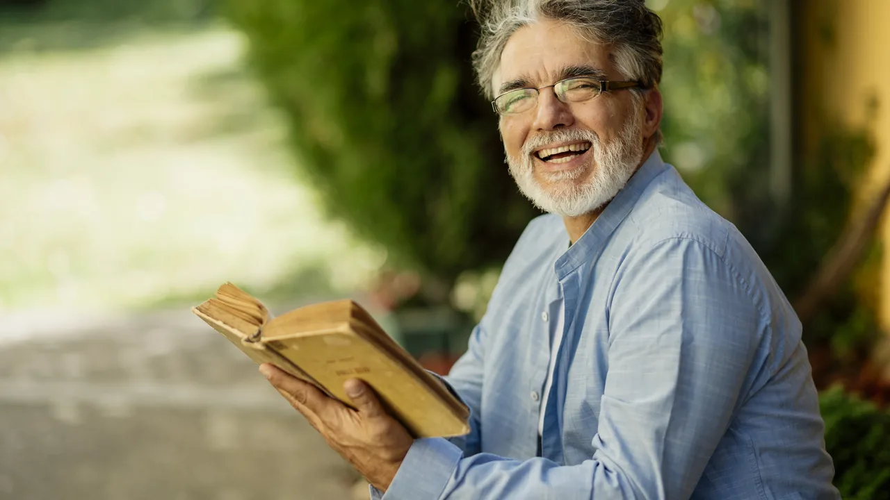 Pessoa idosa segurando um livro em ambiente externo, em imagem editorial sobre prioridade especial