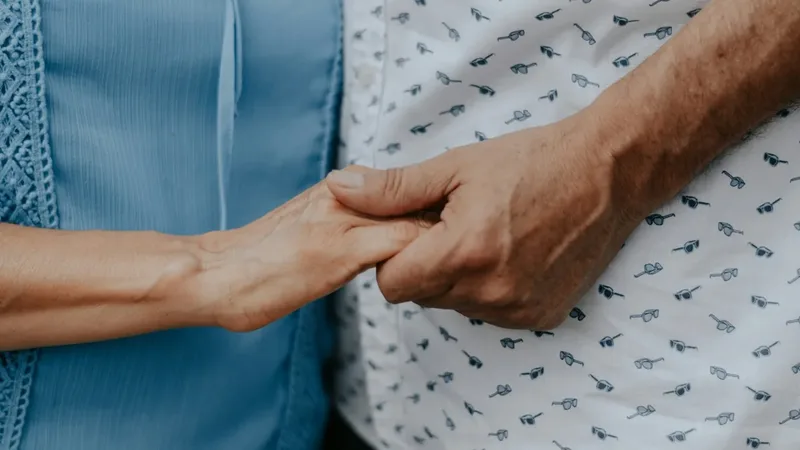 Mãos de uma pessoa cuidadora apoiando as mãos de uma pessoa idosa durante uma conversa ou cuidado em casa
