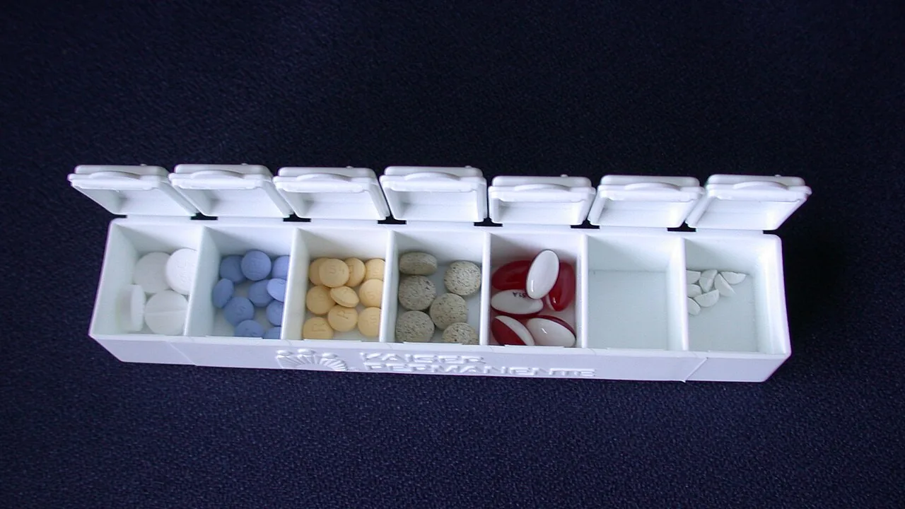 Caixa organizadora de medicamentos aberta com comprimidos separados em compartimentos