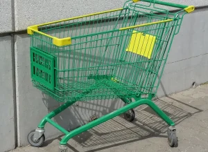 Carrinho de supermercado com rodas, visto de lado, em área externa.