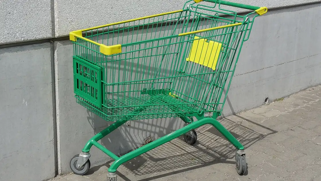 Carrinho de supermercado com rodas, visto de lado, em área externa.