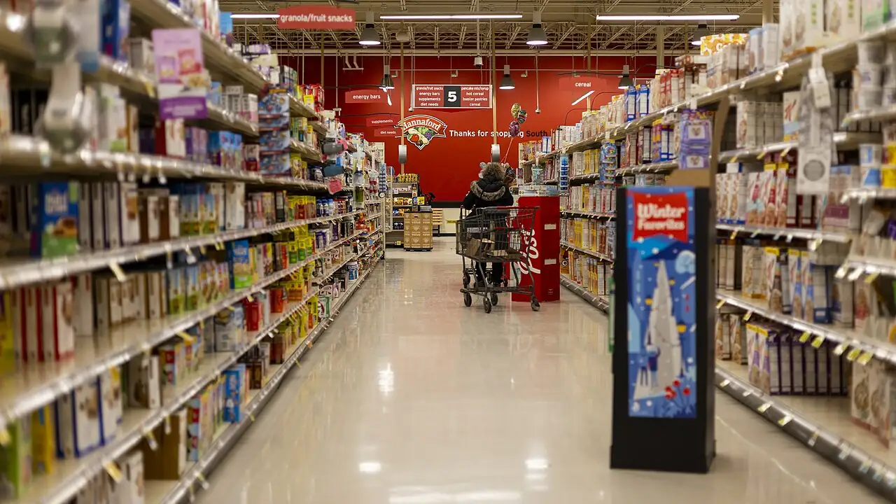 Corredor de supermercado com prateleiras e um carrinho ao centro.