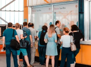 Pessoas aguardam atendimento em uma bilheteria, representando uma fila de serviço ao público.