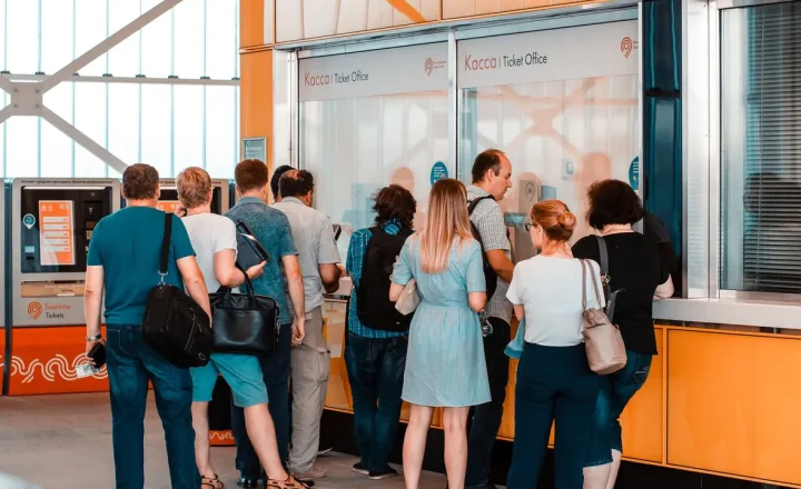 Pessoas aguardam atendimento em uma bilheteria, representando uma fila de serviço ao público.