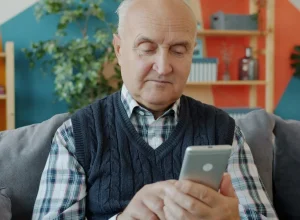 Homem idoso usando o celular sentado em um sofá
