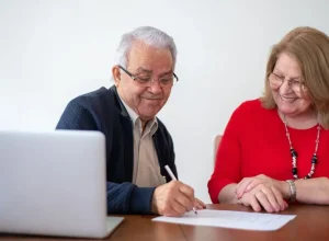 Casal de pessoas idosas assinando documentos à mesa