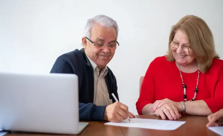 Casal de pessoas idosas assinando documentos à mesa