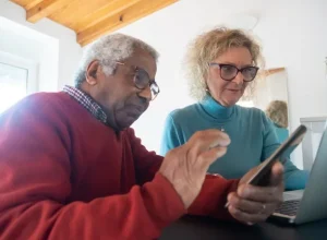 Casal de idosos usando celular e computador em casa