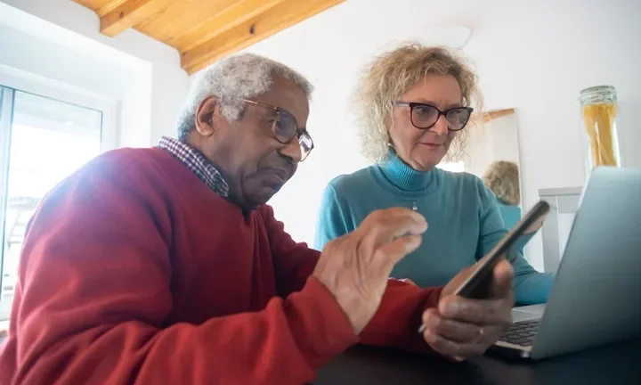 Casal de idosos usando celular e computador em casa